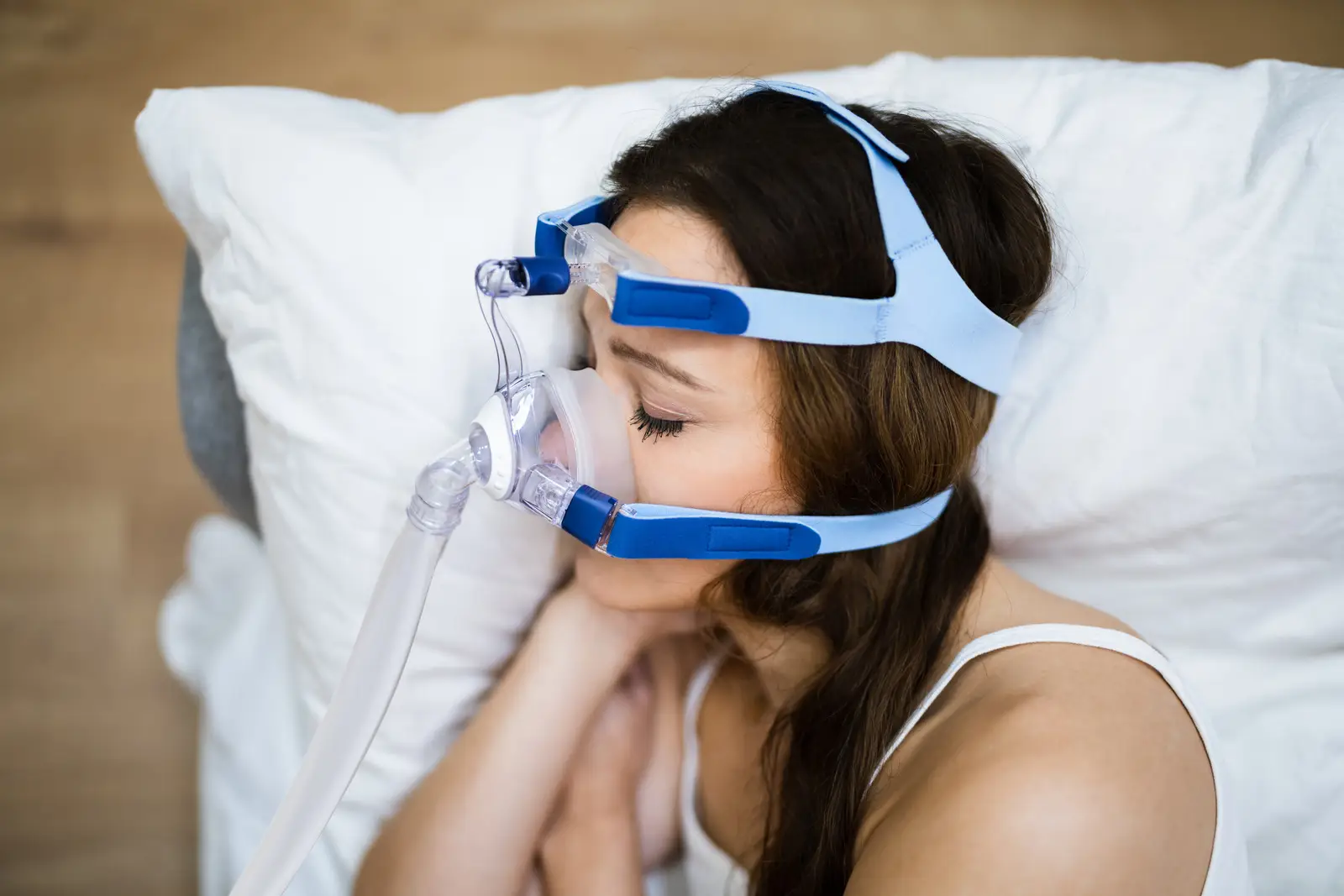 oxysphair-apnee_du_sommeil_esperance_de_vie Femme dormant avec un masque CPAP pour traiter l’apnée du sommeil, allongée sur un oreiller blanc.